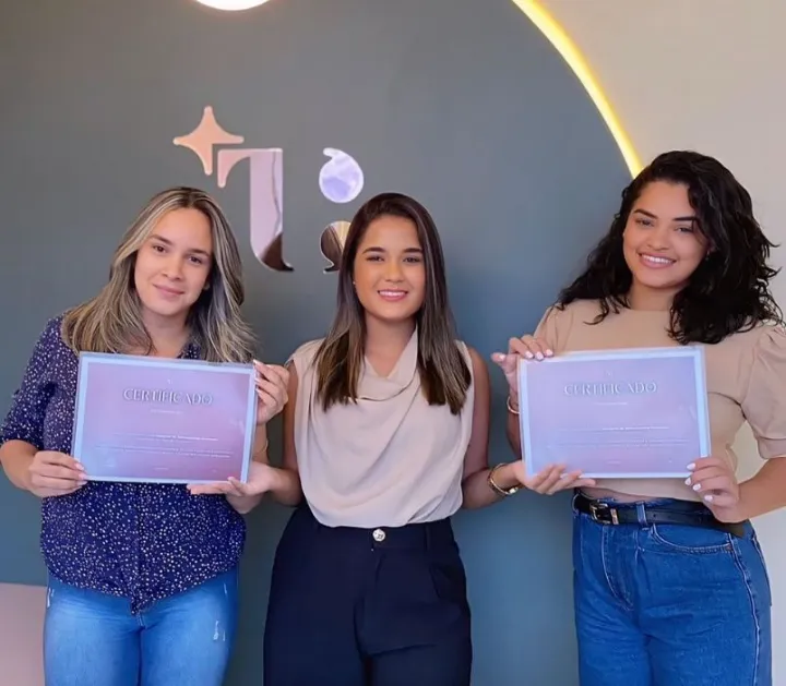 Duas alunas com seus certificados, com a Thainá ao centro